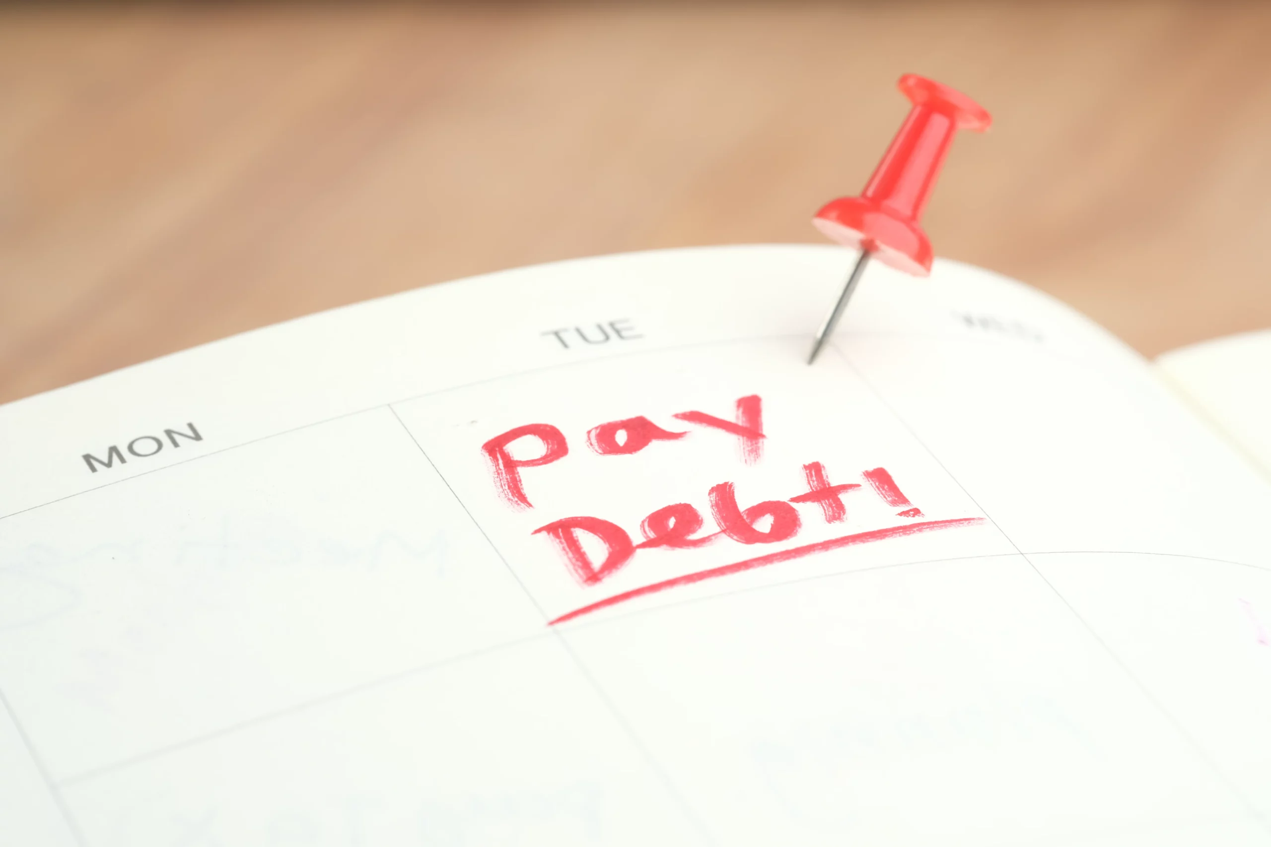 Calendar marked ‘Pay Debt!’ with pushpin, illustrating urgency of addressing debt and considering Chapter 7 bankruptcy filing in Florida.