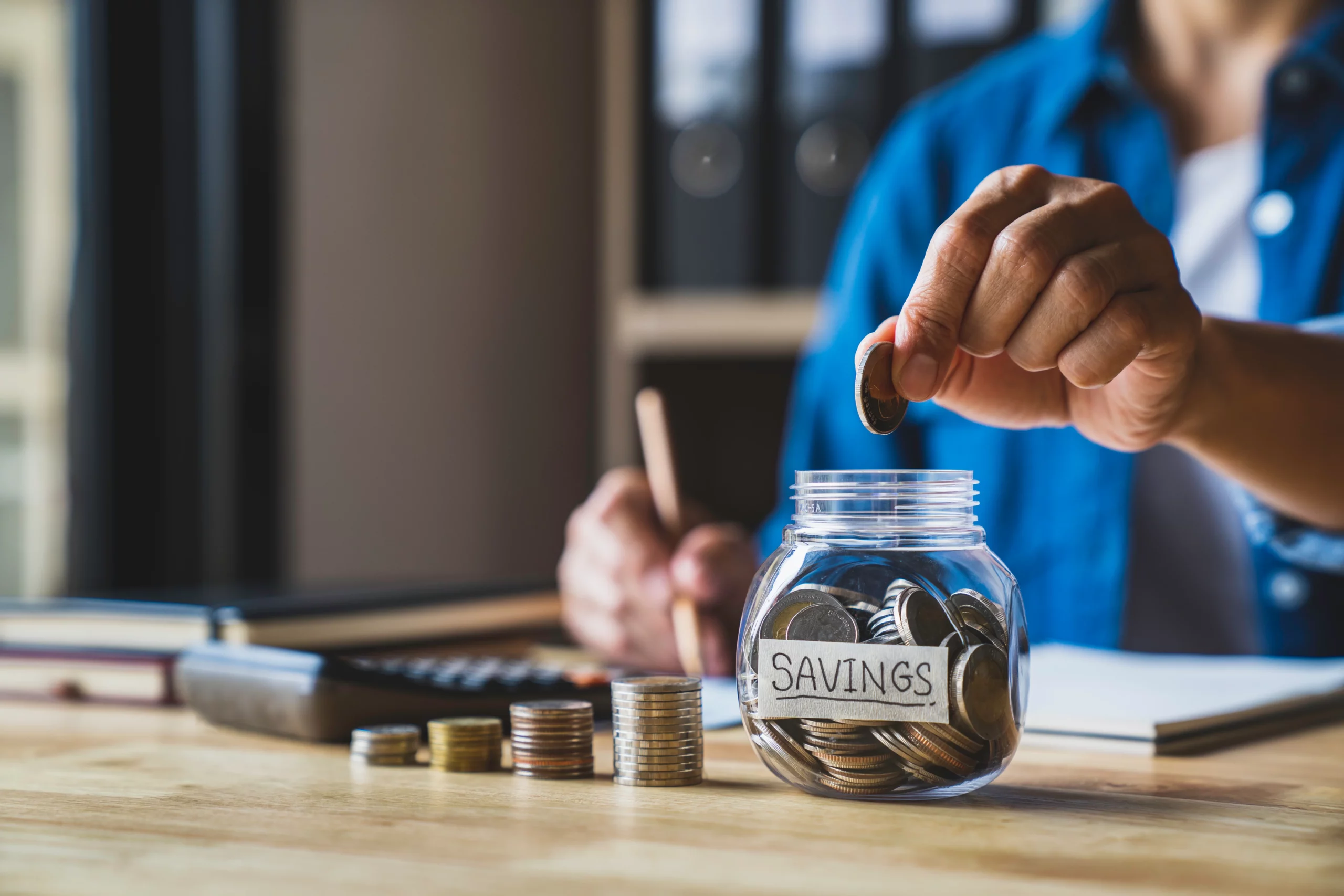 Person adding coin to savings jar at table with calculator and documents, illustrating budgeting and comparing Chapter 7 bankruptcy vs debt settlement financial planning in Florida